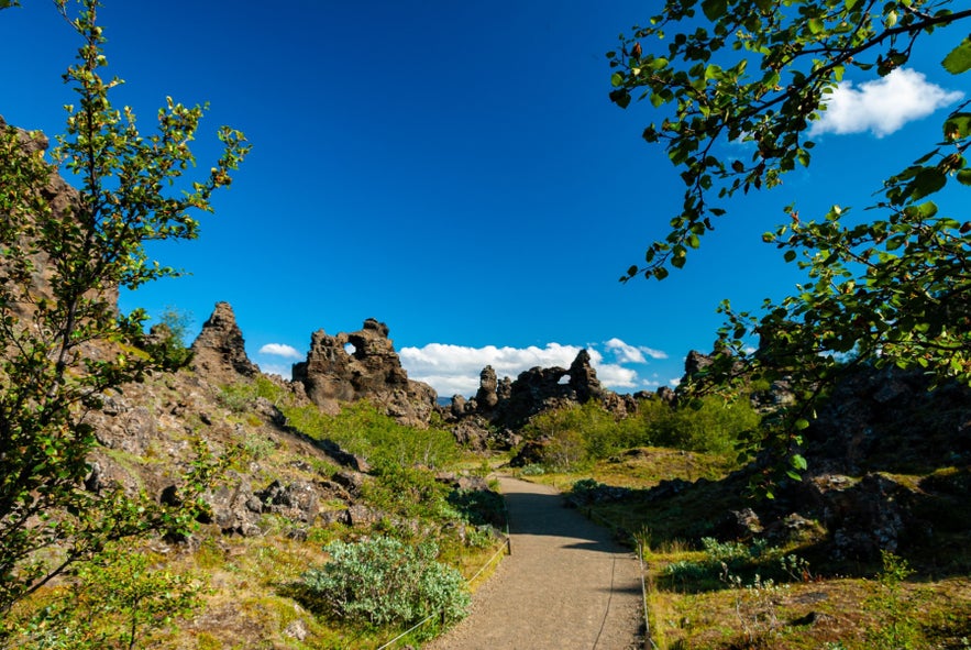Walking path through Dimmuborgir Lava Formations near Lake Myvatn in North Iceland, surrounded by volcanic rock towers and greenery.