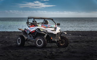 Two travelers on a buggy tour on Solheimasandur, riding on the black sand with the Atalantic behind them.