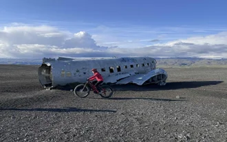 Cyclist rides past the abandoned DC-3 Plane Wreck on Solheimasandur Black Sand Beach in South Iceland.