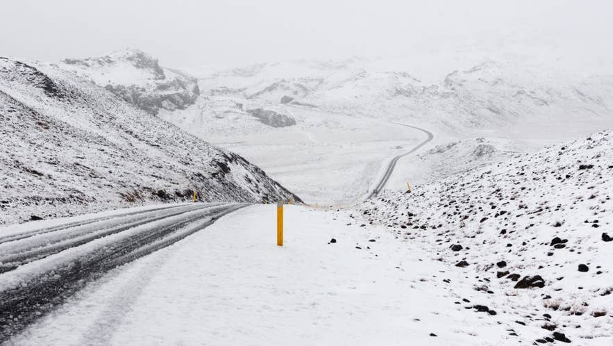 冬季雾天，积雪覆盖的蜿蜒道路穿过冰岛山脉。