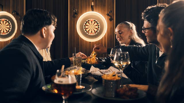 Friends sharing food and drinks at Brons Keflavik restaurant, enjoying Icelandic dining with dartboards and a lively atmosphere.