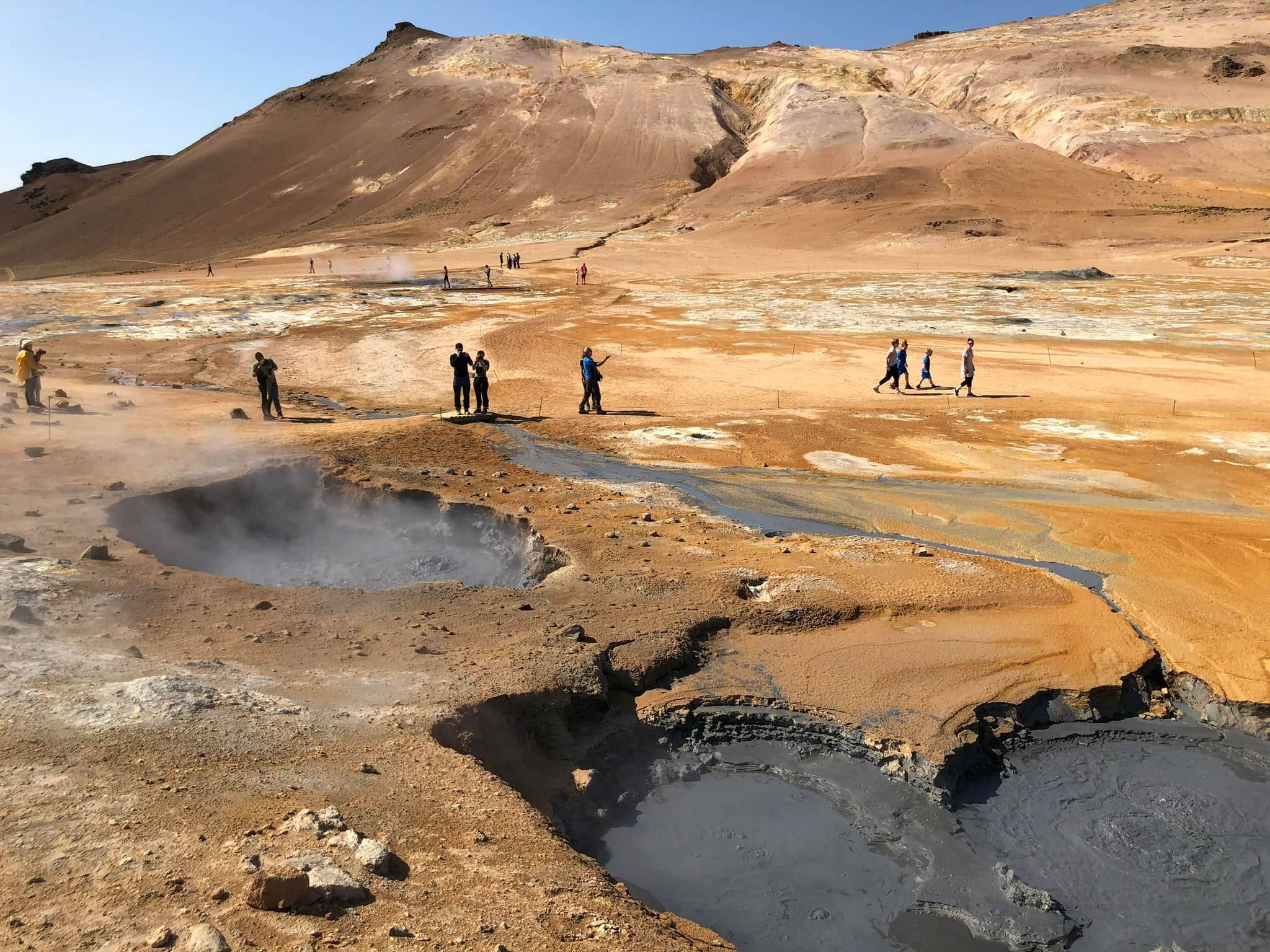 Boiling mud pots and steaming vents in Namaskard Geothermal Area in North Iceland with barren orange hills.