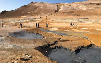 Boiling mud pots and steaming vents in Namaskard Geothermal Area in North Iceland with barren orange hills.