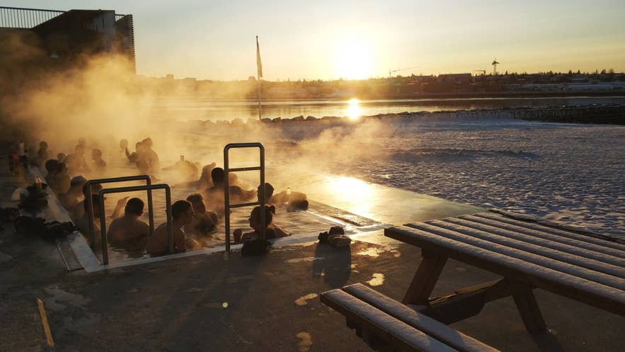 Geothermisches Freibad in Reykjavik mit Badenden bei Sonnenuntergang.