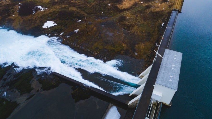 Hydropower plant in Iceland with turquoise glacial river and dam infrastructure.