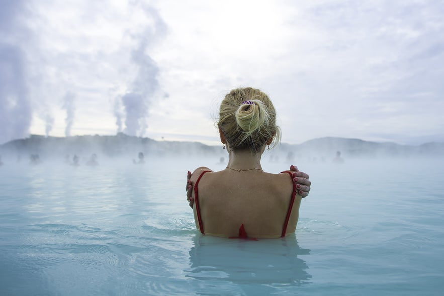 Visitor soaking in the Blue Lagoon in Iceland while keeping hair out of the mineral-rich water to protect it
