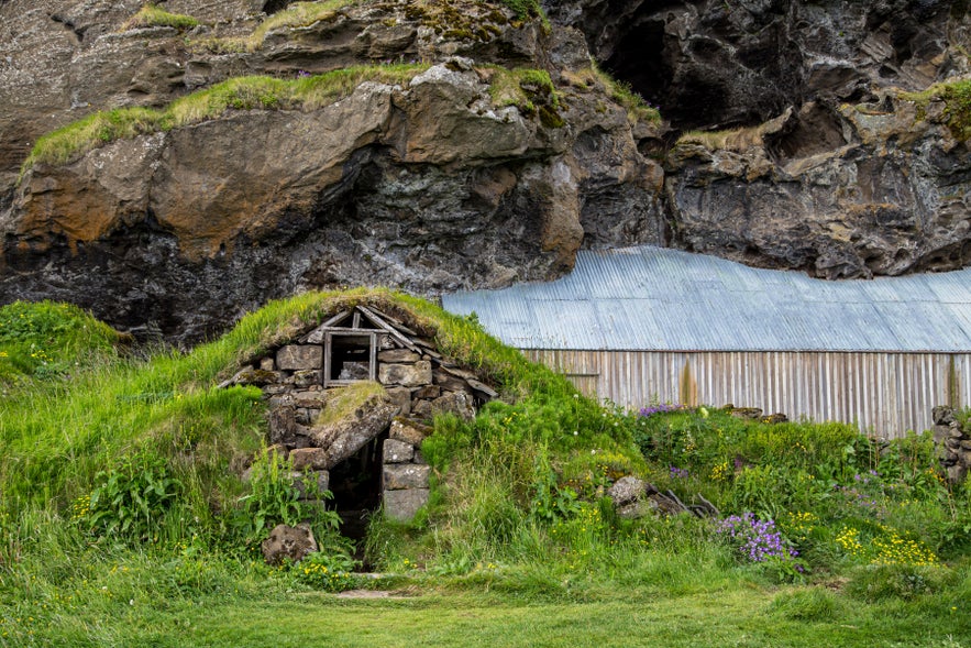 Dranginn elf rock in South Iceland with traditional turf structure built into a rocky cliff face.