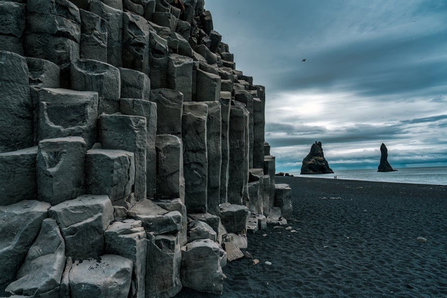 Reynisfjara black sand beach with basalt columns and Reynisdrangar sea stacks, legendary troll formations in South Iceland.