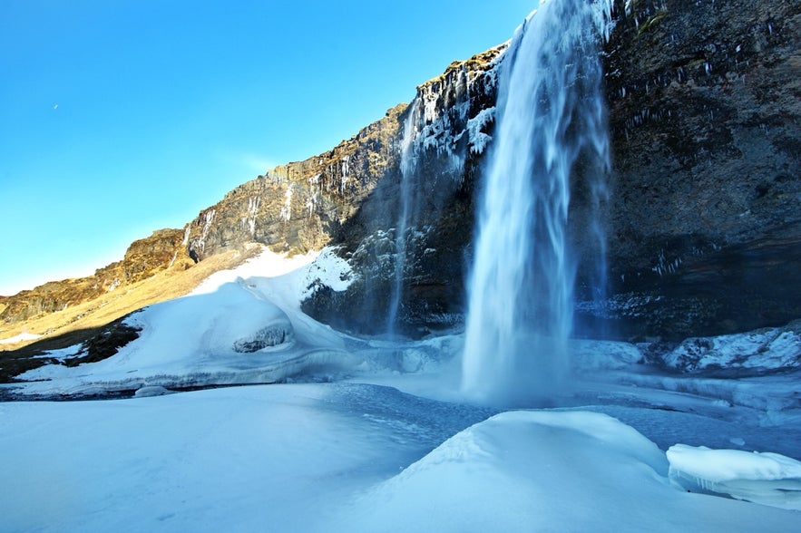The sun shines over one side of Seljalandsfoss Waterfall in winter.