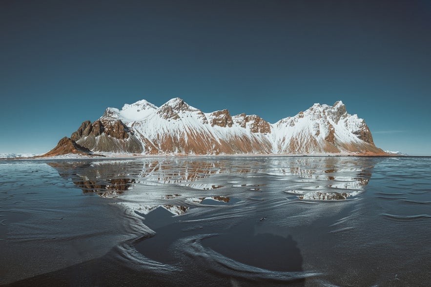 Snow-covered Vestrahorn mountains reflecting on the icy shore at Stokksnes beach, South East Iceland