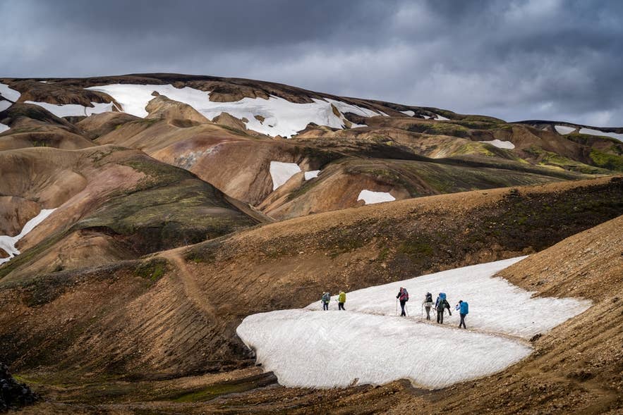 Hikers crossing a snow patch in the Icelandic Highlands, a colder climate than the coast even in summer.