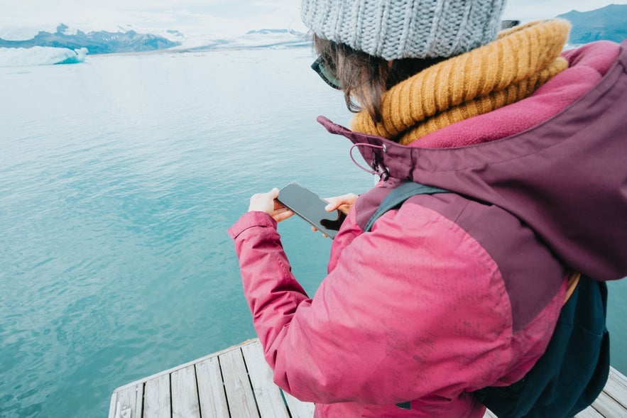 A woman checks her phone while exploring icy landscapes in Iceland.