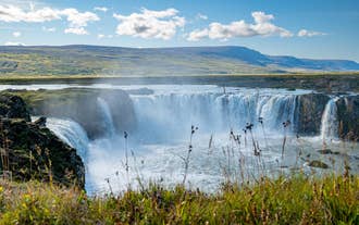Vista diurna della cascata Godafoss che si getta in una gola rocciosa sotto un cielo azzurro.