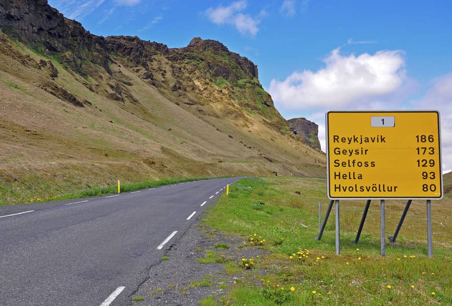 A yellow Icelandic road sign on Route 1 lists distances to Reykjavik, Geysir, and nearby towns.