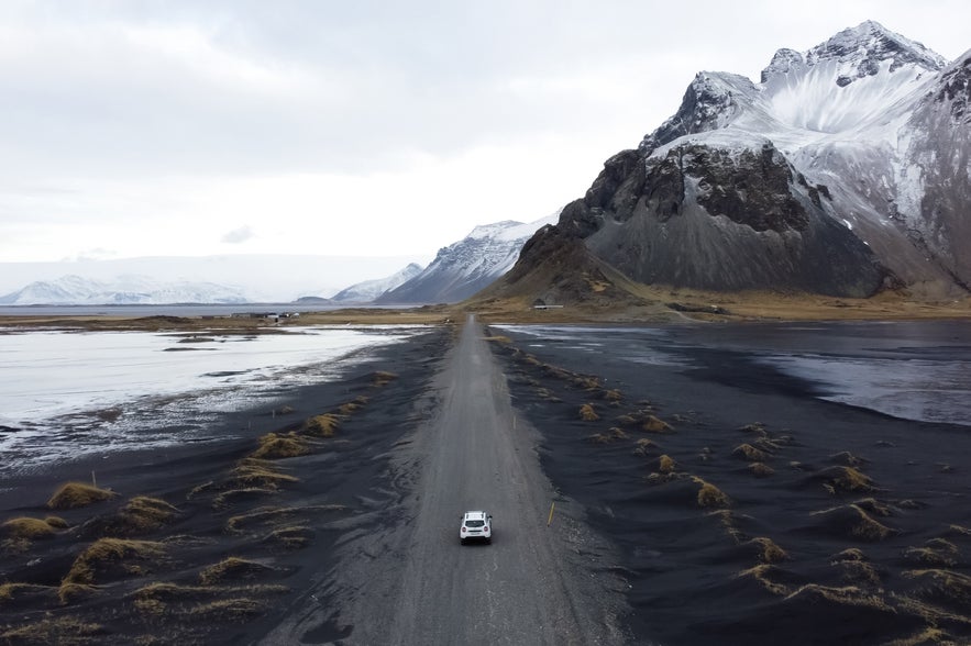 Car driving across a black sand landscape covered in snow in Iceland.