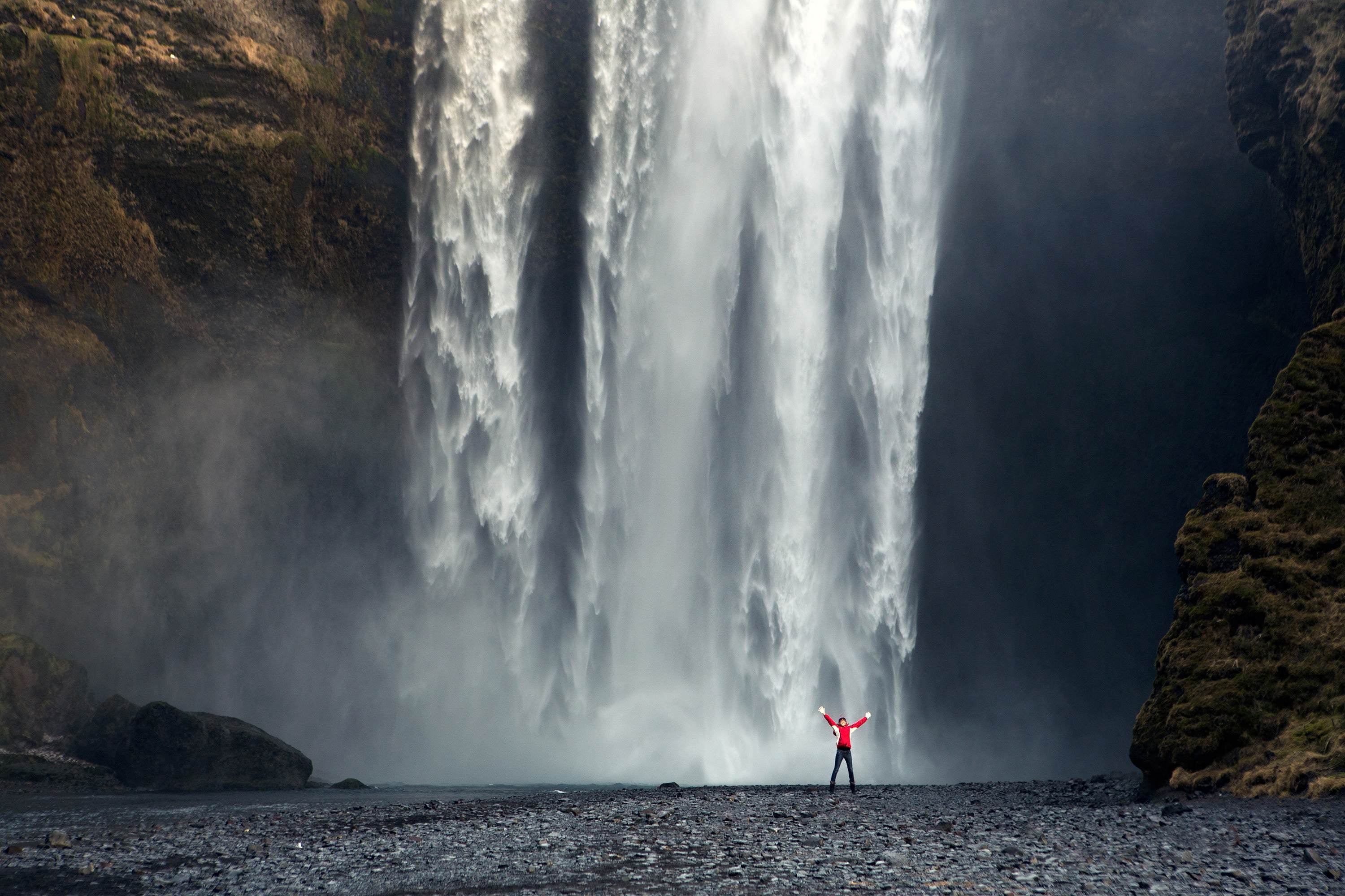 A traveler posing in front of the mighty cascade of the Skogafoss waterfall.