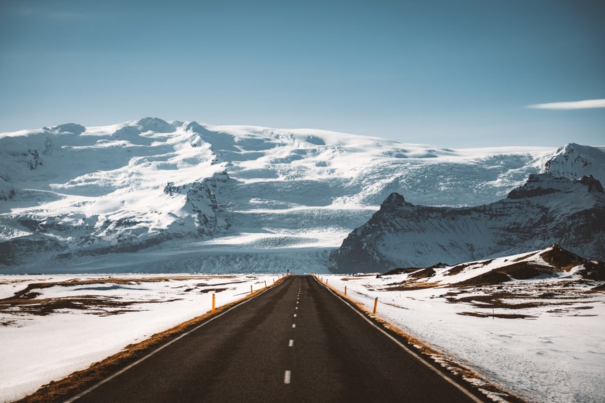 Snowy landscape with a clear road stretching toward mountains in Iceland.