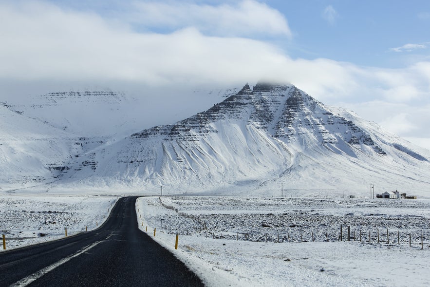 Clear winter road with snow-covered sides and mountains ahead in Iceland.
