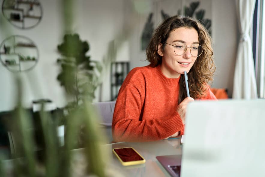Woman in a red sweater studying Icelandic language on a laptop at a desk with a smartphone nearby