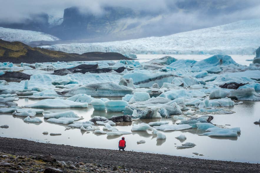 Eine Person sitzt an der Gletscherlagune Fjallsarlon.