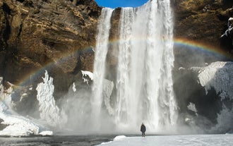 A rainbow forms by the icy cliffs and valley of Skogafoss Waterfall.