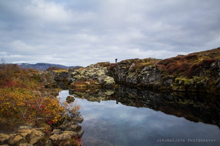 Thingvellir National Park in Iceland with calm rift valley lake, mossy lava rocks, and autumn landscape under cloudy skies.