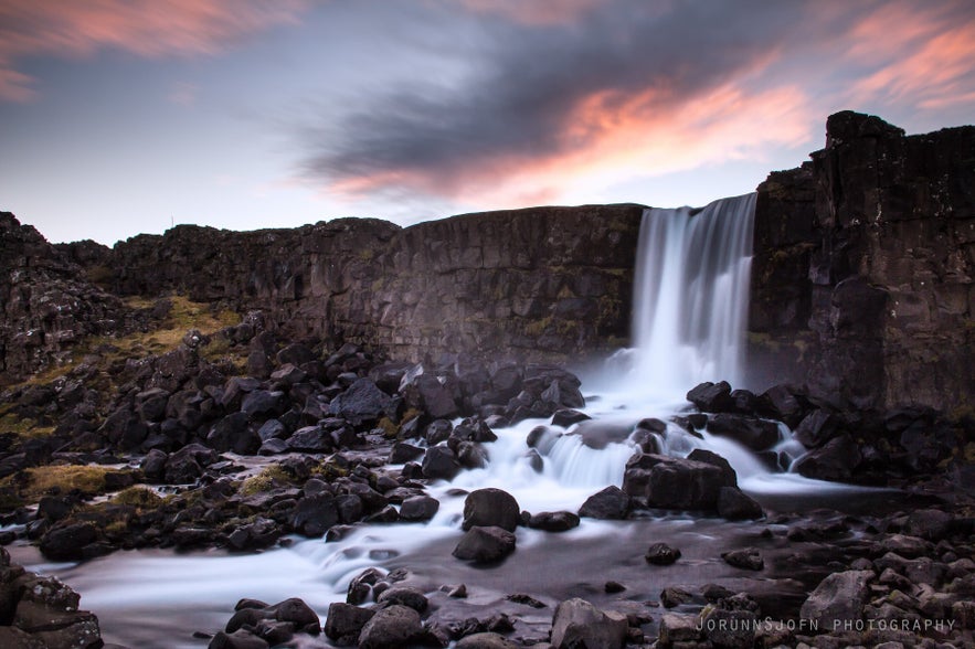 Oxararfoss waterfall in Thingvellir National Park, Iceland, flowing over rocky cliffs at sunset with silky river water.