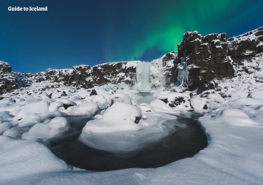 Oxararfoss waterfall in Iceland frozen over during winter with northern lights above it