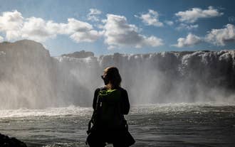 Eine Frau posiert für ein Foto mit dem Dettifoss im Hintergrund.