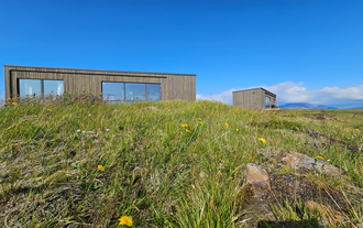 Exterior view of Hitarneskot Accommodation surrounded by grassy hills in West Iceland.