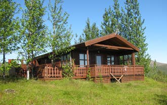 Wooden cabin surrounded by trees and grassy hills, typical of Uthlid Cottages in the Golden Circle.