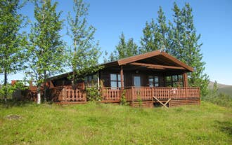 Wooden cabin surrounded by trees and grassy hills, typical of Uthlid Cottages in the Golden Circle.