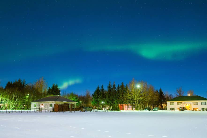 Northern lights over Hvolsvollur, South Iceland, with village homes and snowy fields along the South Coast at night.