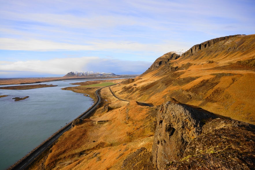 A coastal road winds below golden hills along Iceland&rsquo;s South Coast on a clear day.