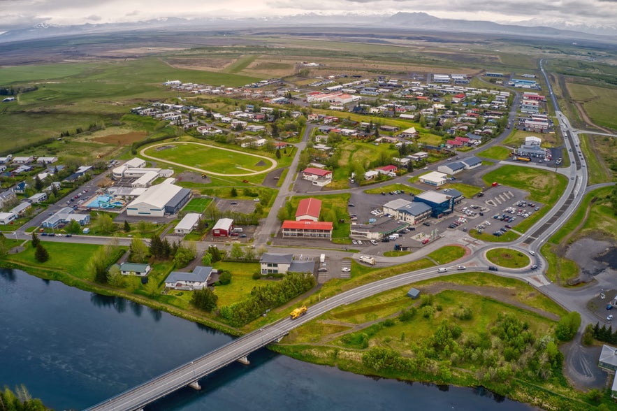 Aerial view of Hella town in South Iceland, featuring its bridge, swimming pool, residential area, and countryside.