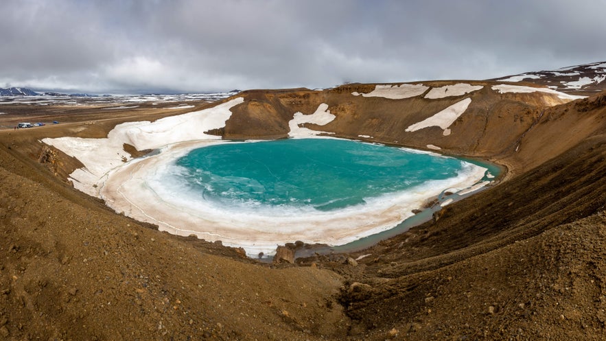 Viti Crater in Iceland&rsquo;s Krafla volcanic area with turquoise water and patches of snow under a cloudy sky.