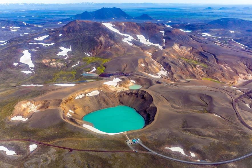 冰岛北部克拉夫拉破火山口内，维蒂火山口的蓝色湖水、周围的火山地貌与斑驳残雪。