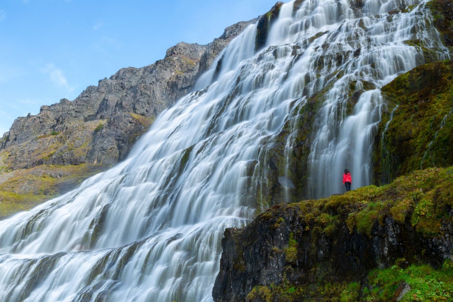 Dynjandi waterfall in Iceland&rsquo;s Westfjords, with cascading tiers and a hiker standing near the base in early autumn