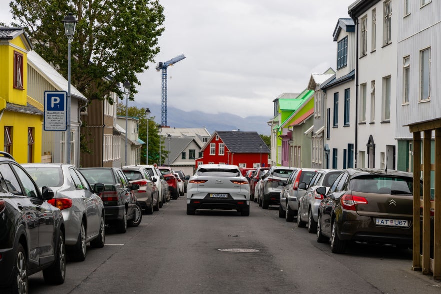 Rental car driving through a residential street in Reykjavik, showing city parking and colorful Icelandic houses
