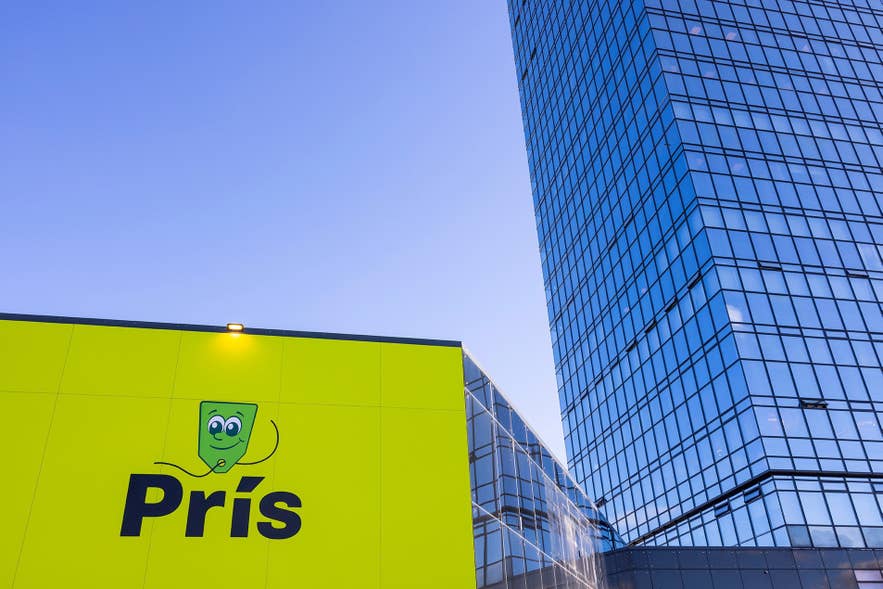 ทางเข้าร้าน Prís สีเหลืองเขียวข้างอาคารกระจก Turninn ใน Kopavogur ท้องฟ้าสีน้ำเงินเข้ม