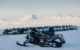A parked snowmobile rests on the snowy plains of Langjokull Glacier, with distant mountain peaks in the background.
