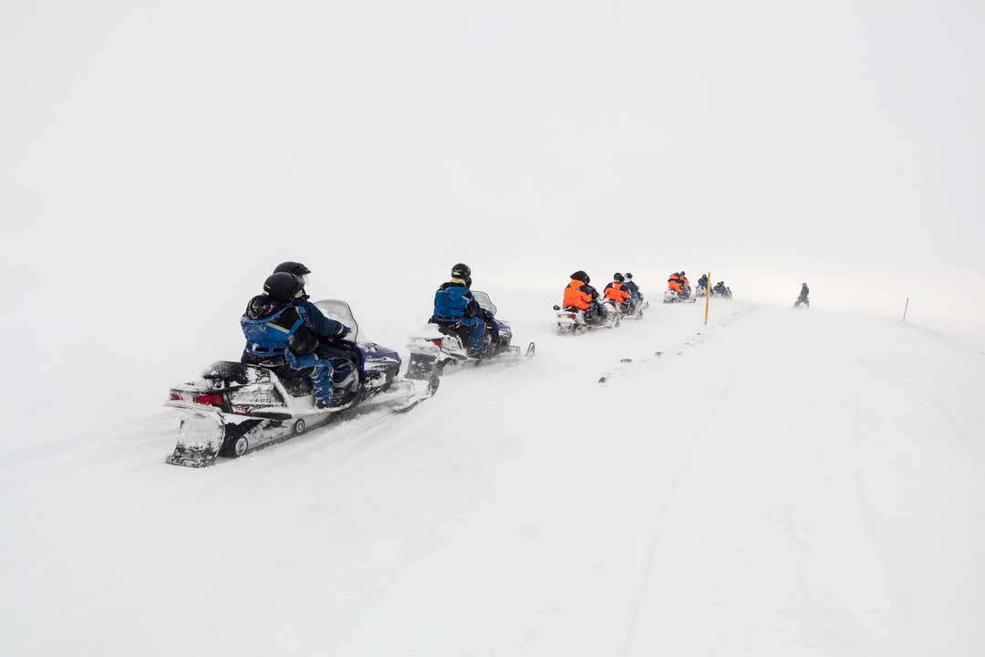 Group riding snowmobiles on Langjokull Glacier in heavy snow, part of the thrilling glacier adventure experience in Iceland.