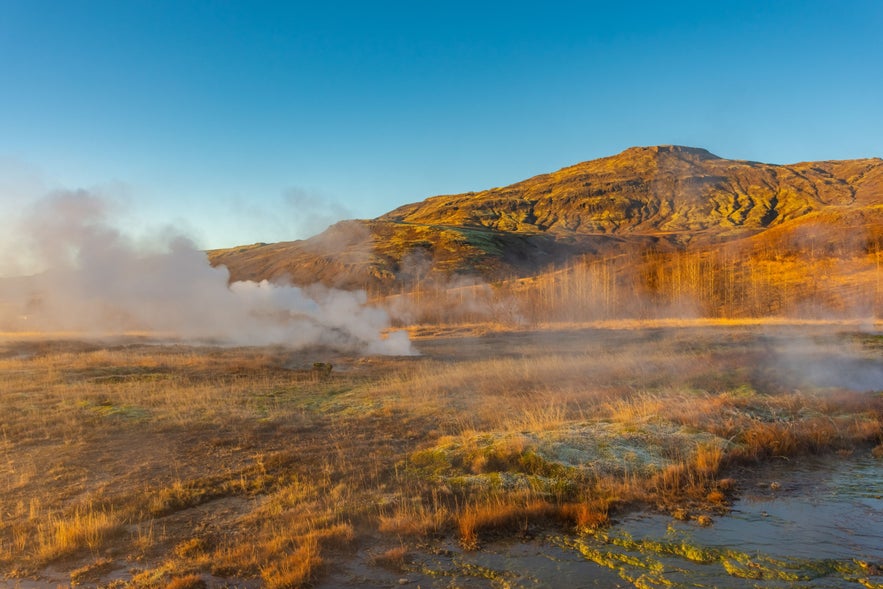 Steaming geothermal landscape in Haukadalur Geothermal Valley, Iceland, with steam vents and volcanic hills.