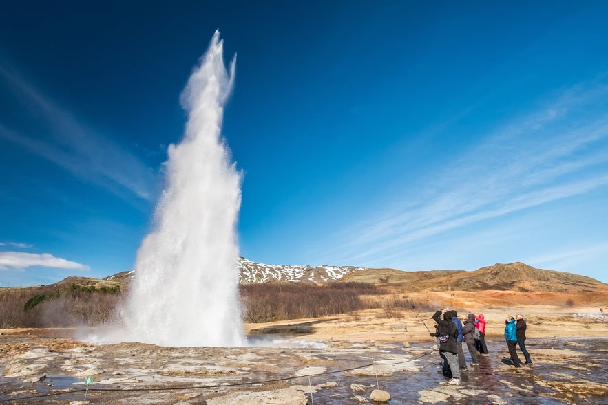 Strokkur geyser erupting as visitors watch in Haukadalur Geothermal Valley, Iceland.