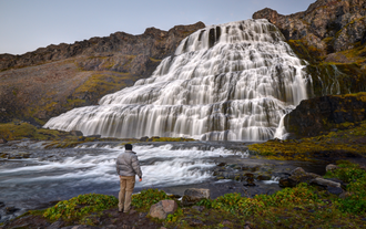 A hiker standing in front of the magnificent Dynjandi Waterfall in Iceland.
