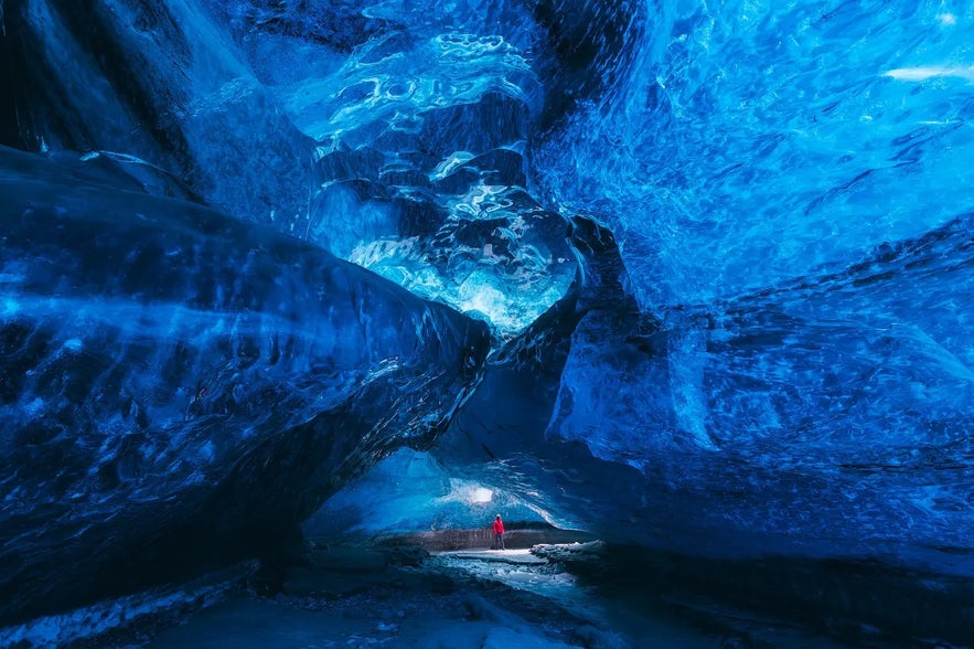 A person in a red jacket stands inside a blue ice cave in Vatnaj&ouml;kull Glacier, Iceland.