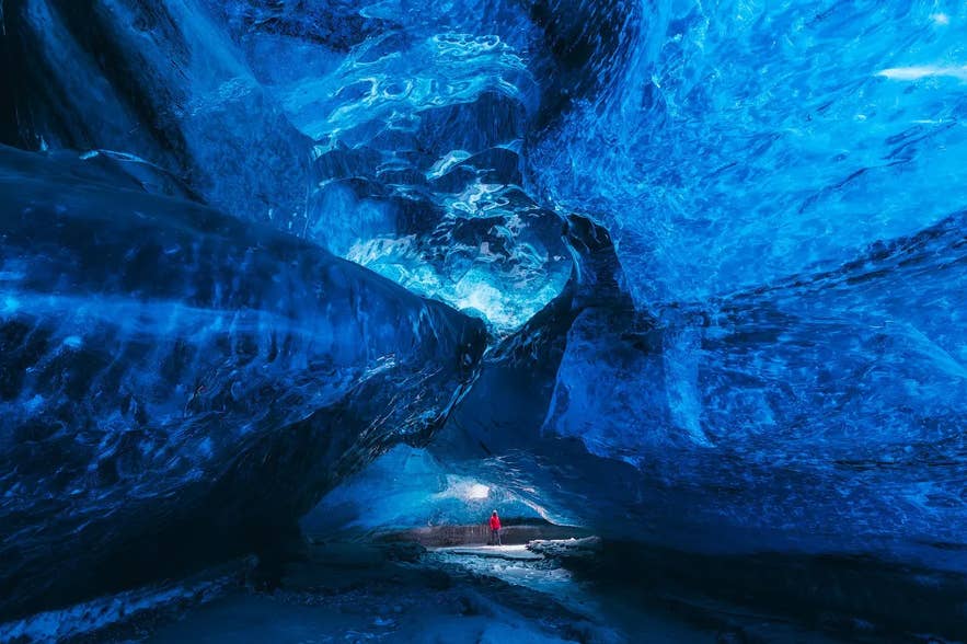 A person in a red jacket stands inside a blue ice cave in Vatnajökull Glacier, Iceland. A person in a red jacket stands inside a blue ice cave in Vatnajökull Glacier, Iceland.