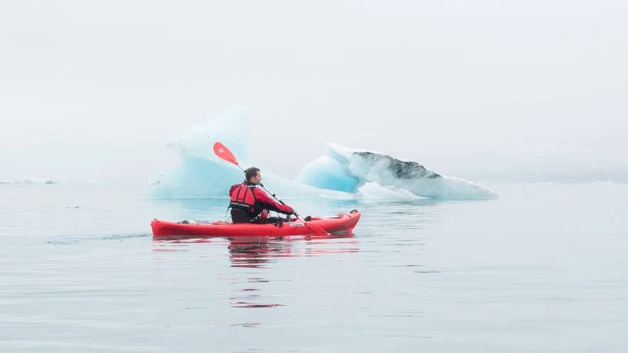 A kayaker paddling through calm waters among floating icebergs in Iceland. A kayaker paddling through calm waters among floating icebergs in Iceland.