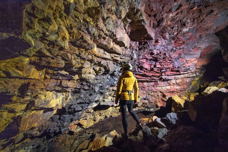 A visitor standing inside a volcanic cave with layered lava rock walls in Iceland.