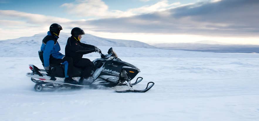 Two people riding a snowmobile across a snowy landscape in Iceland. Two people riding a snowmobile across a snowy landscape in Iceland.